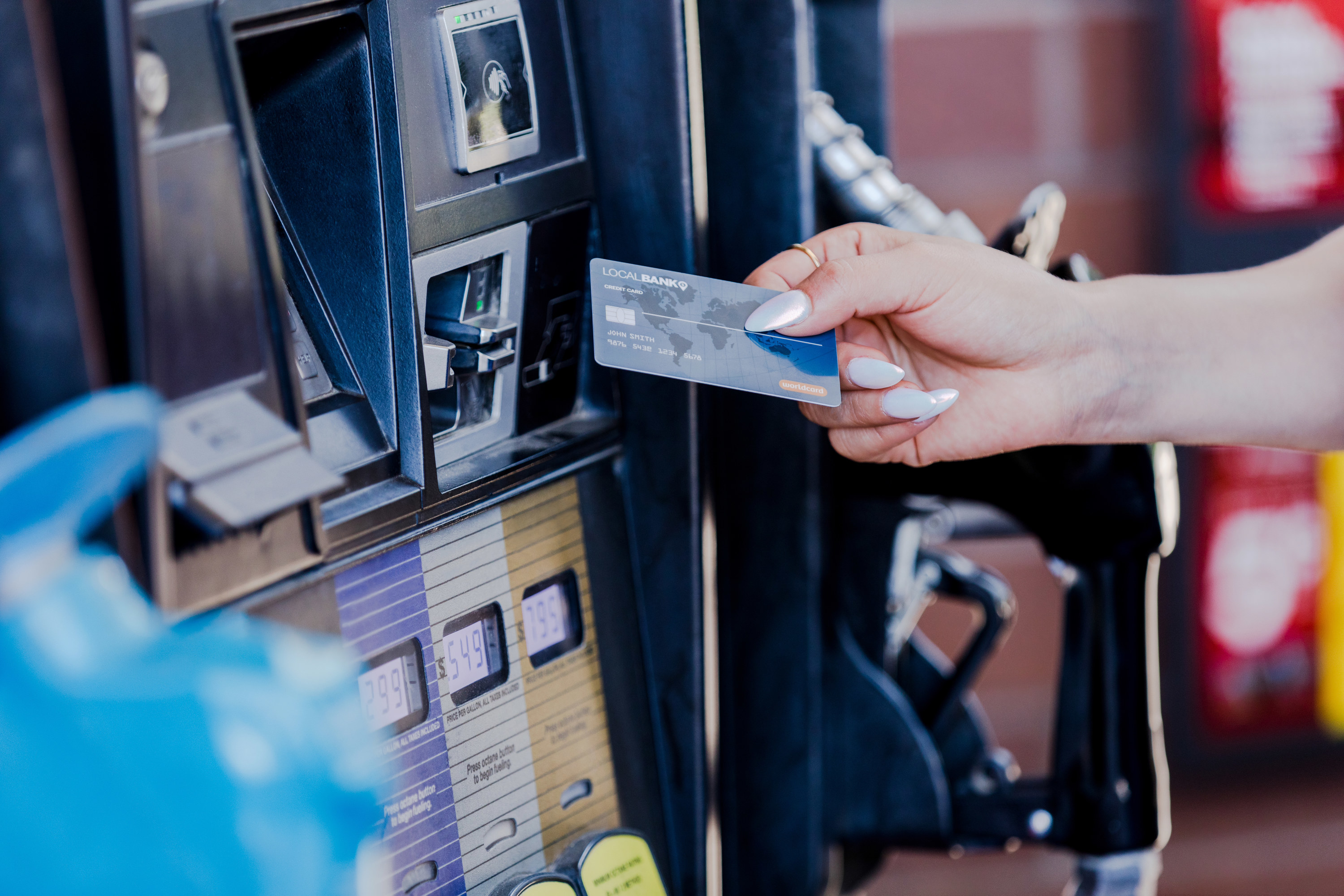 The focus of the photo is on a woman&#x27;s nicely manicured hand as she prepares to pay for gas at the pump