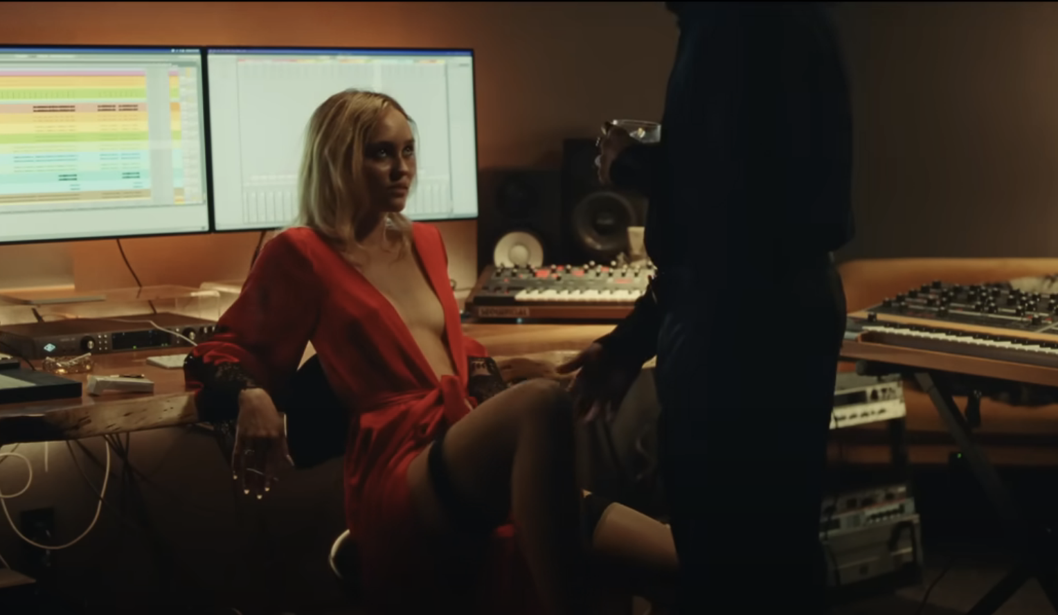 Lily-Rose&#x27;s character sits in a chair in a music studio and looks up while a man standing touches her knee