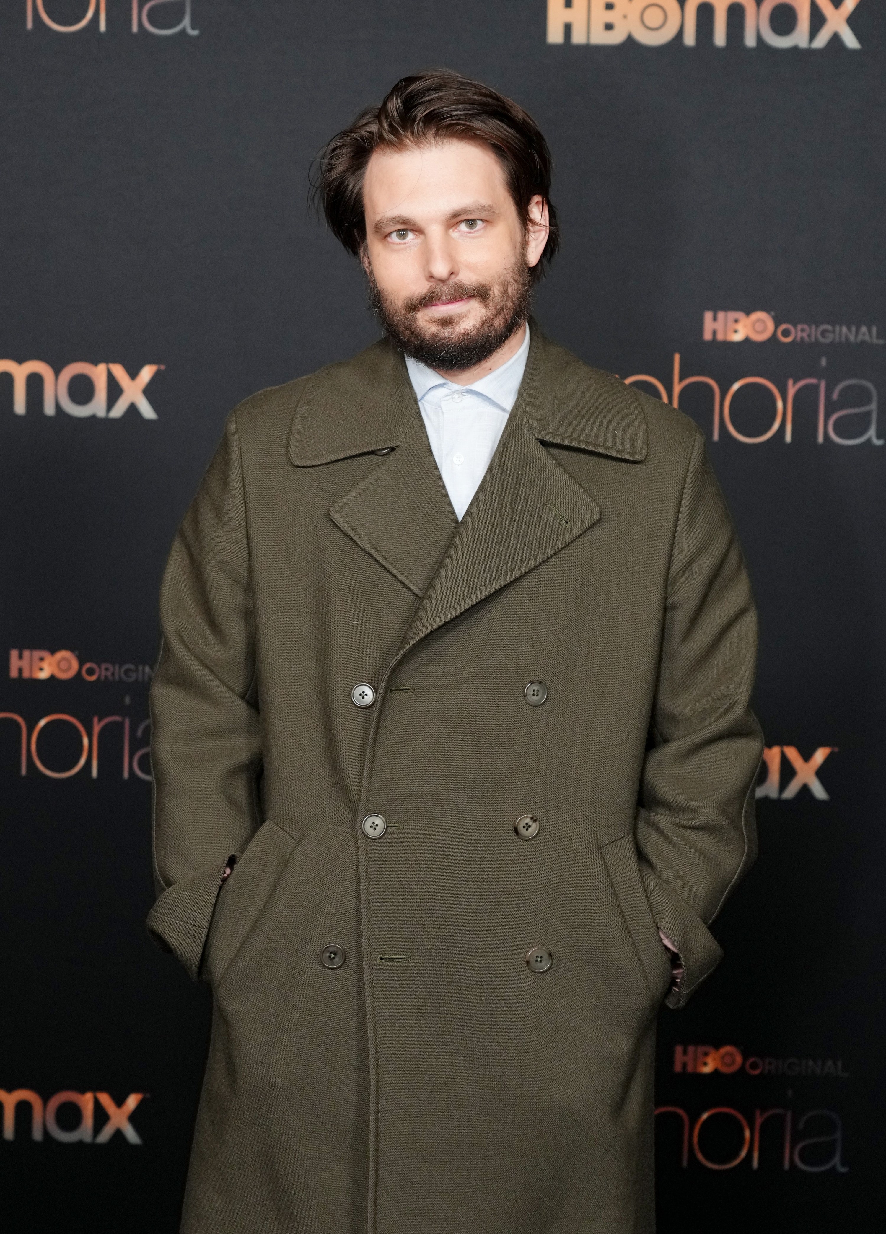 A closeup of Sam Levinson at a Euphoria event wearing a long coat with his hands in his pocket