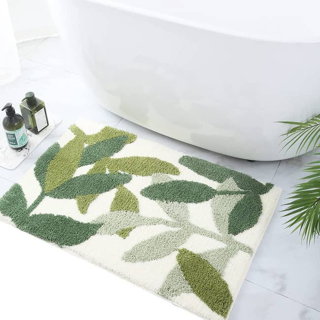 A white bath mat with leaves in three shades of green in front of a bathtub