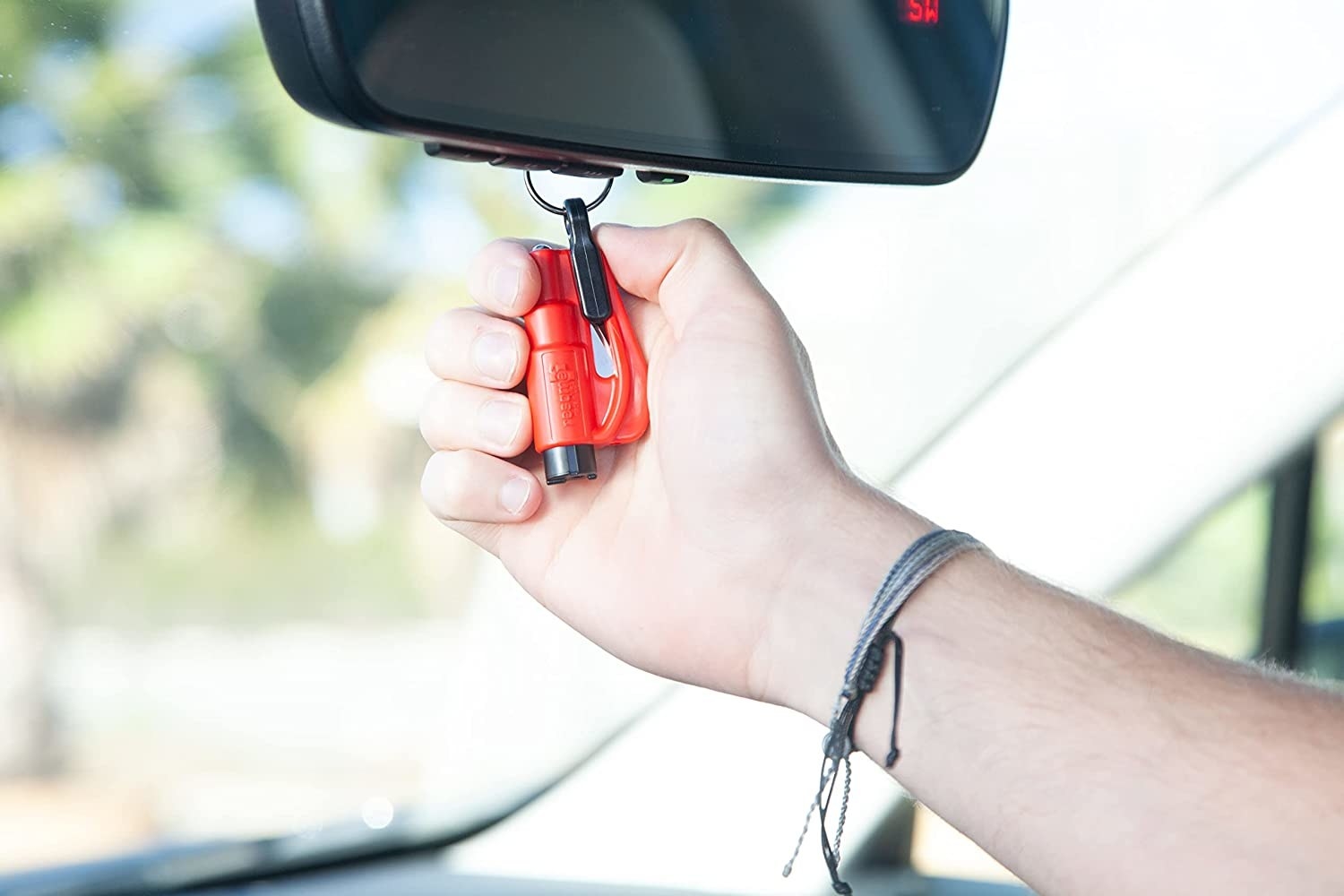 Model gripping the keychain which is hooked to the rearview mirror in a car