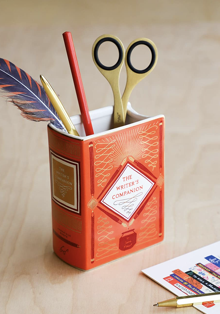 the book vase on a desk with pens and pencils in it