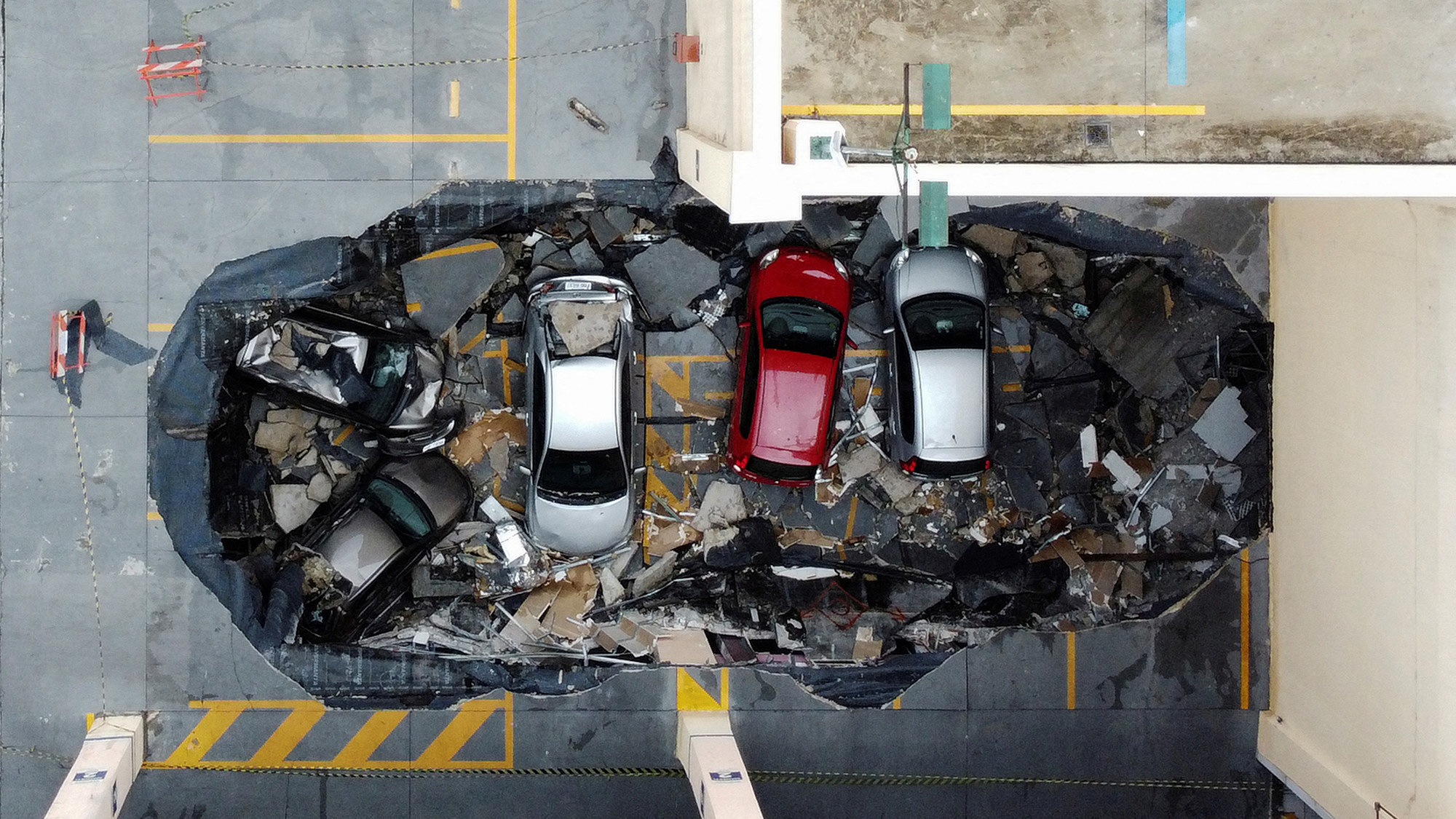 A row of crashed cars in a concrete sinkhole surrounded by rubble