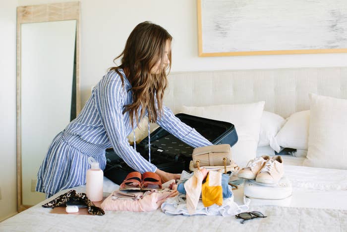 blogger packing clothes and accessories into their suitcase