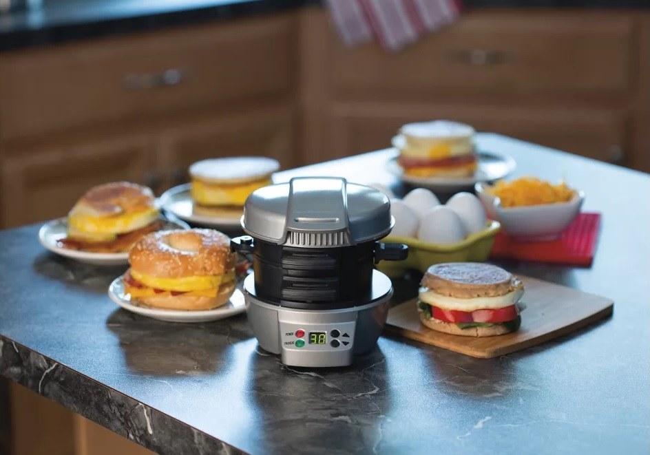 The sandwich maker on a counter surrounded by breakfast sandwiches