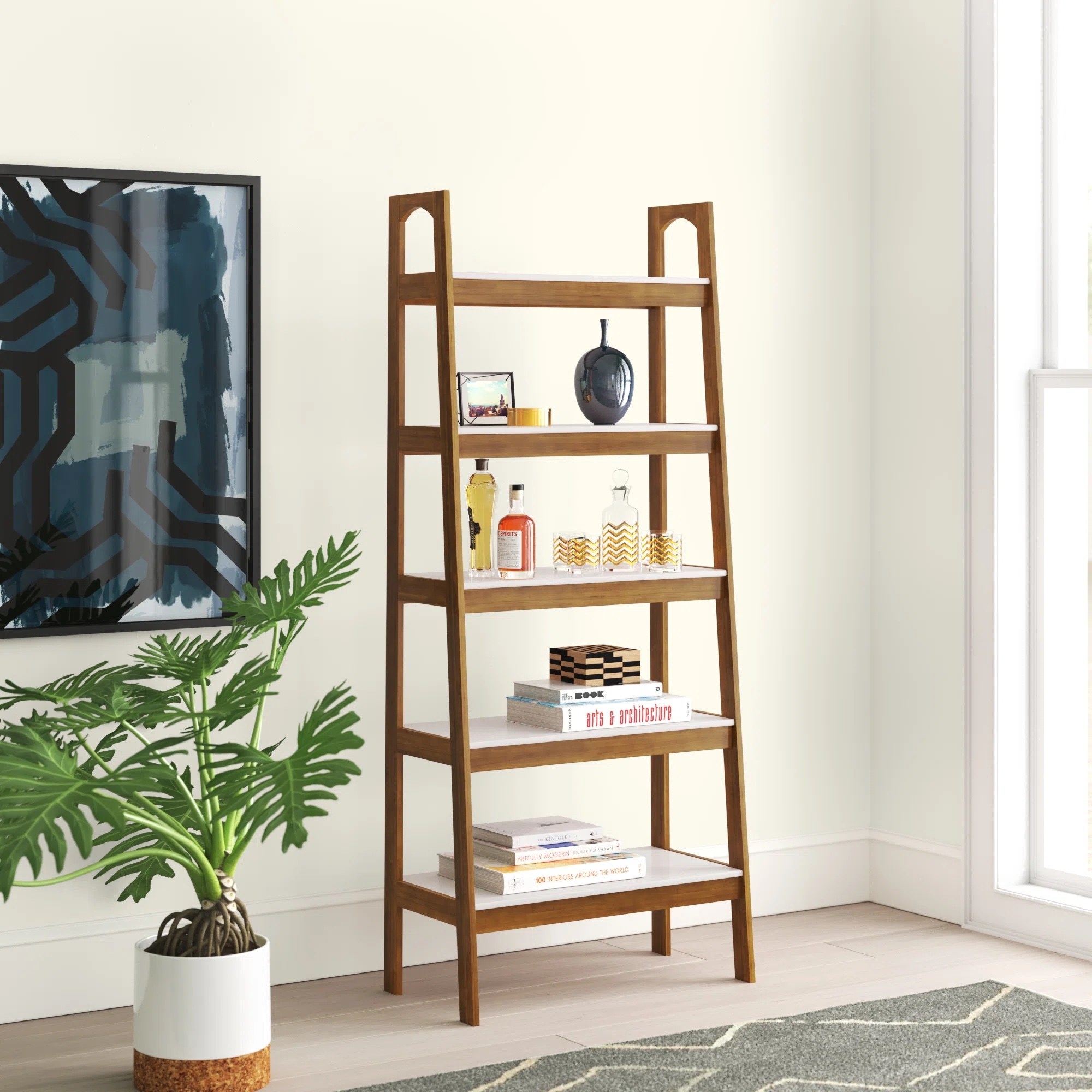 a solid wood ladder bookcase in brown holding cocktail glasses and coffee table books