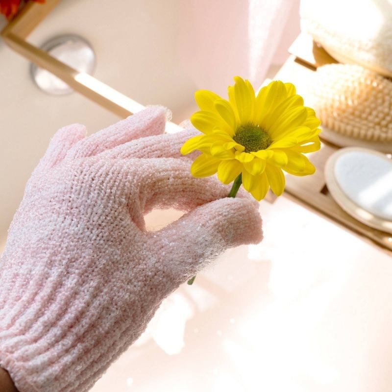 A person wearing an exfoliating glove while holding a sunflower