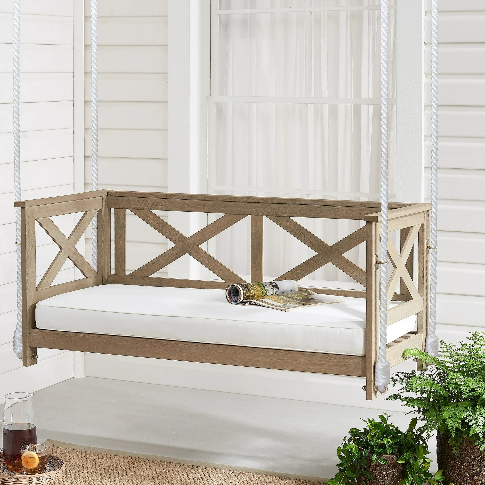 The wooden porch swing with a cushion hanging on a porch