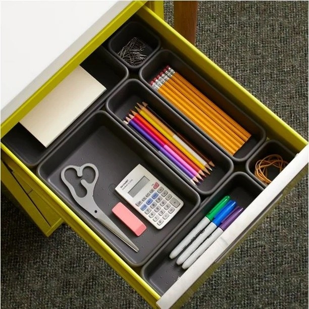 black drawer organizers holding various office supplies inside a drawer