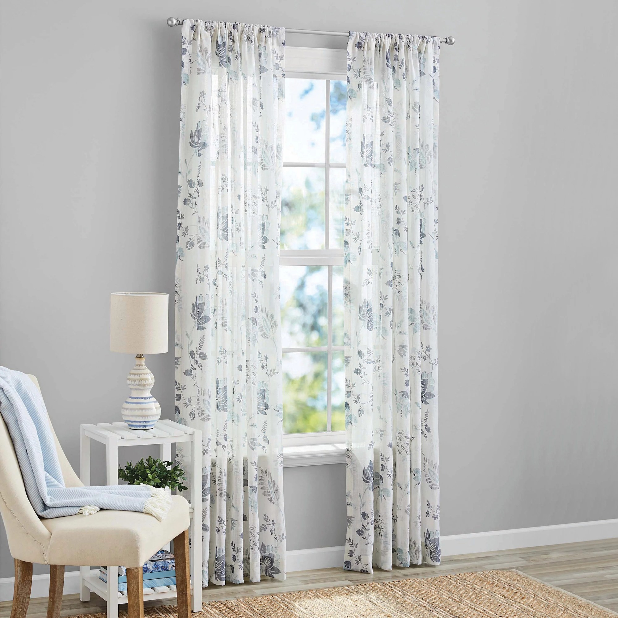 A floral curtain panel on either side of a window letting a fair amount of light in