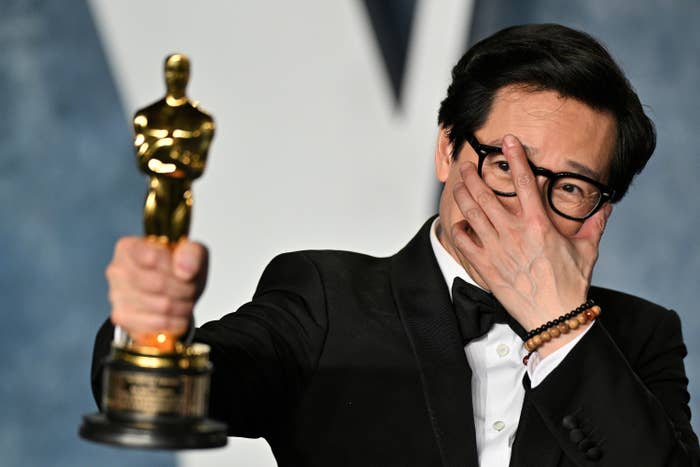 Ke Huy Quan holding his Oscar and adjusting his eyeglasses