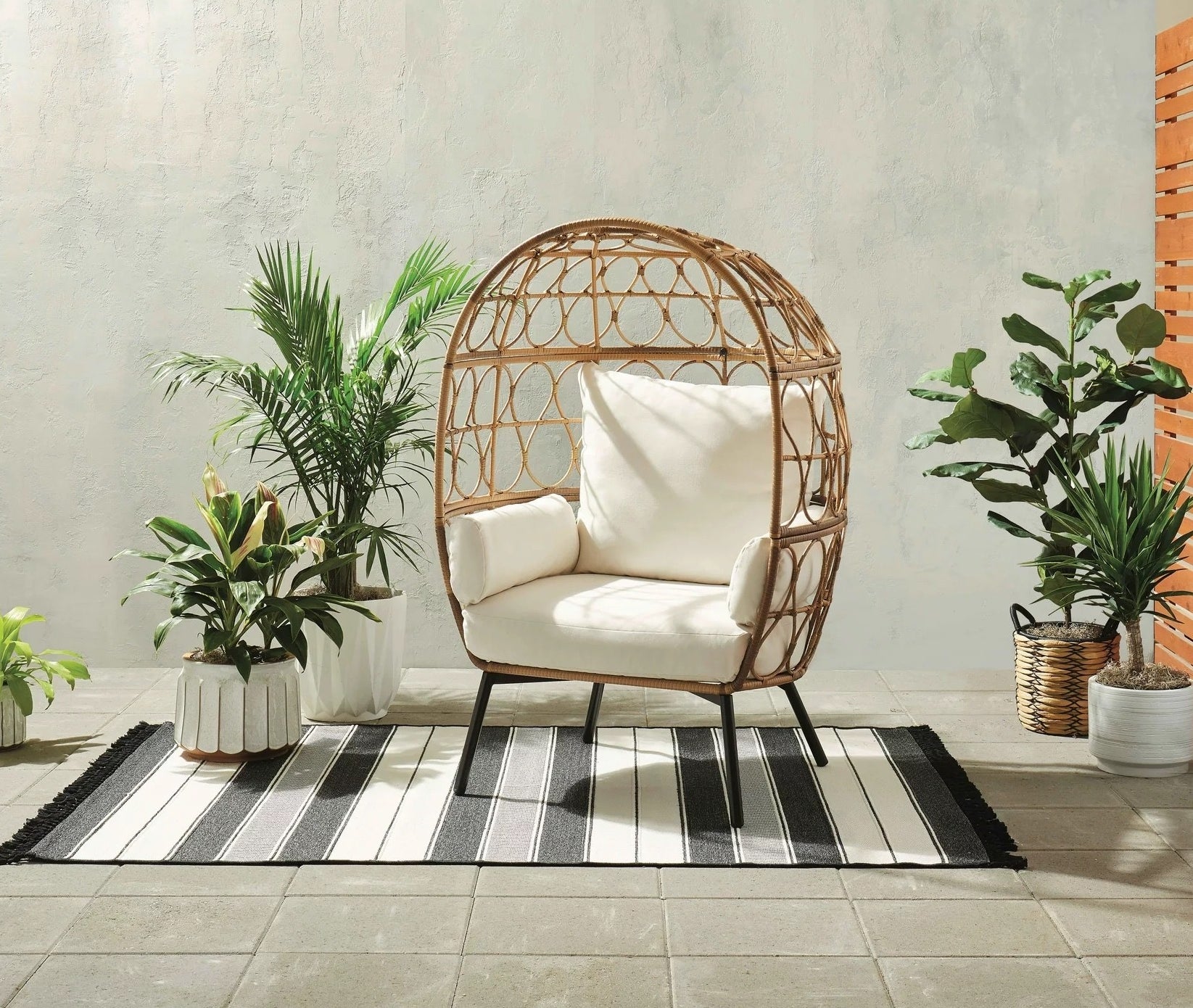 brown wicker egg chair with white cushions in a cute outdoor area