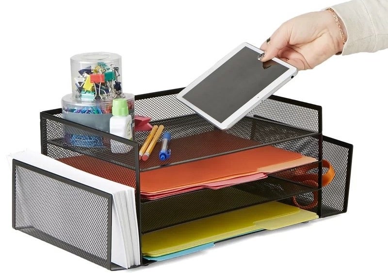 a person putting a tablet down on the four tier shelf with pencils and folders in the organizer