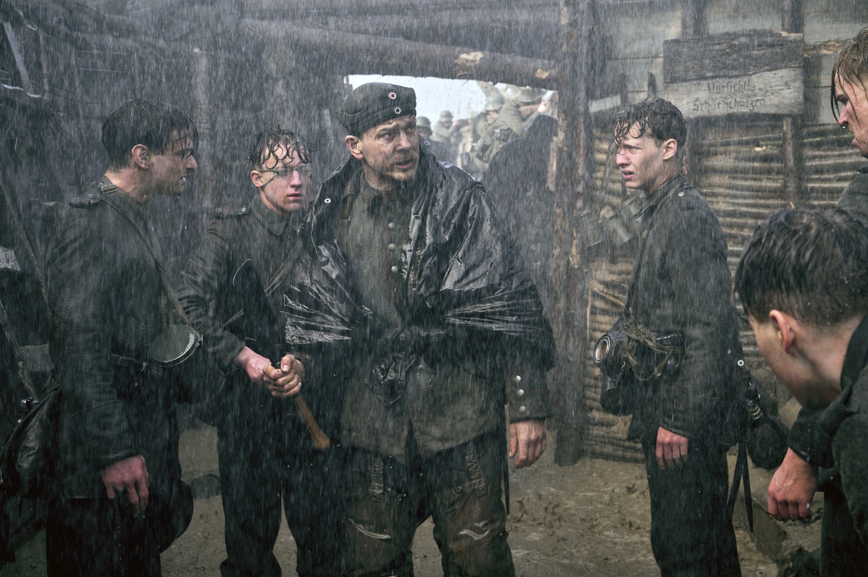 Several soldiers standing in barracks as it rains heavily in a scene from All Quiet on the Western Front