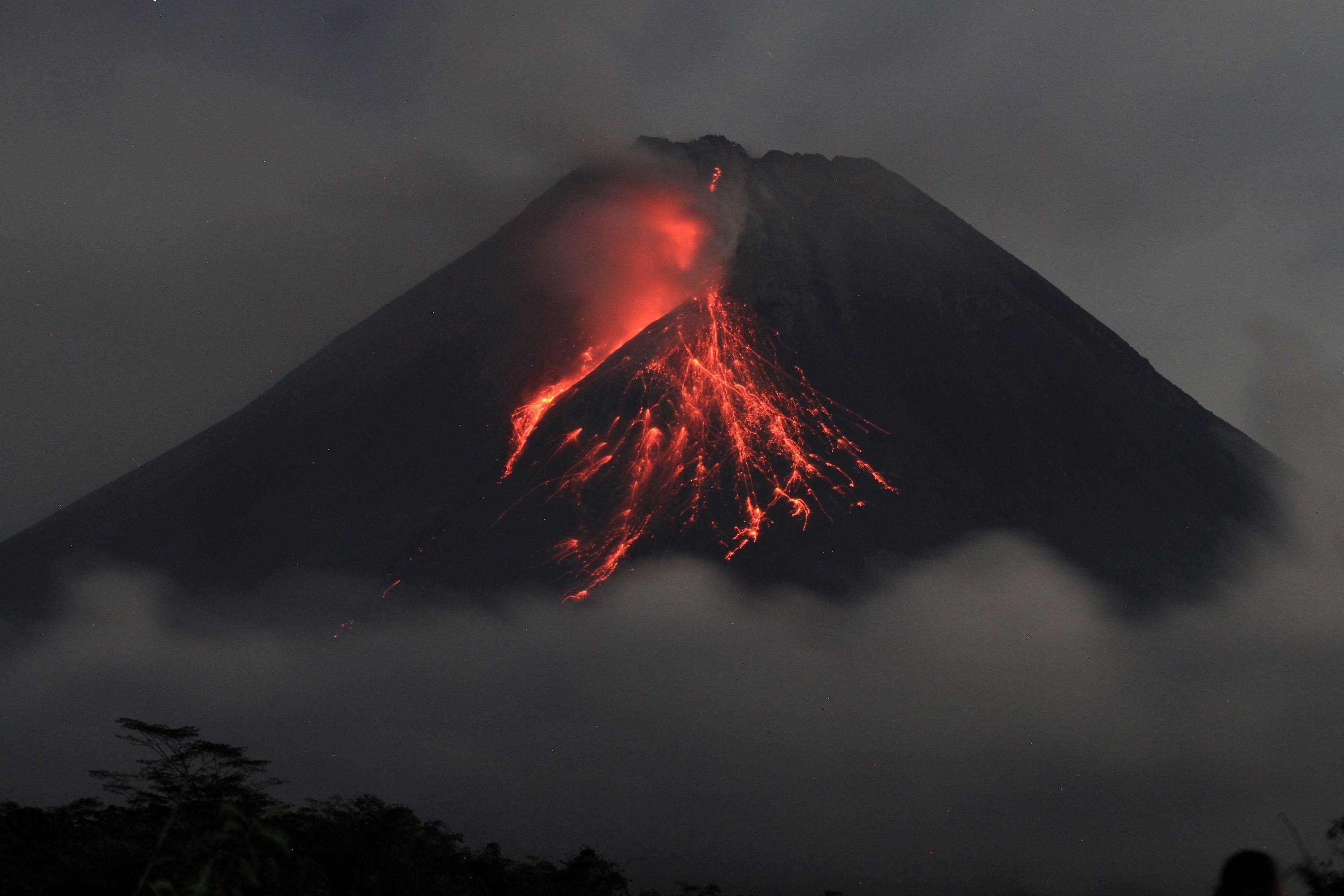 Lava erupts from Mount Merapi, sliding down the side in a red blaze of sparks and smoke