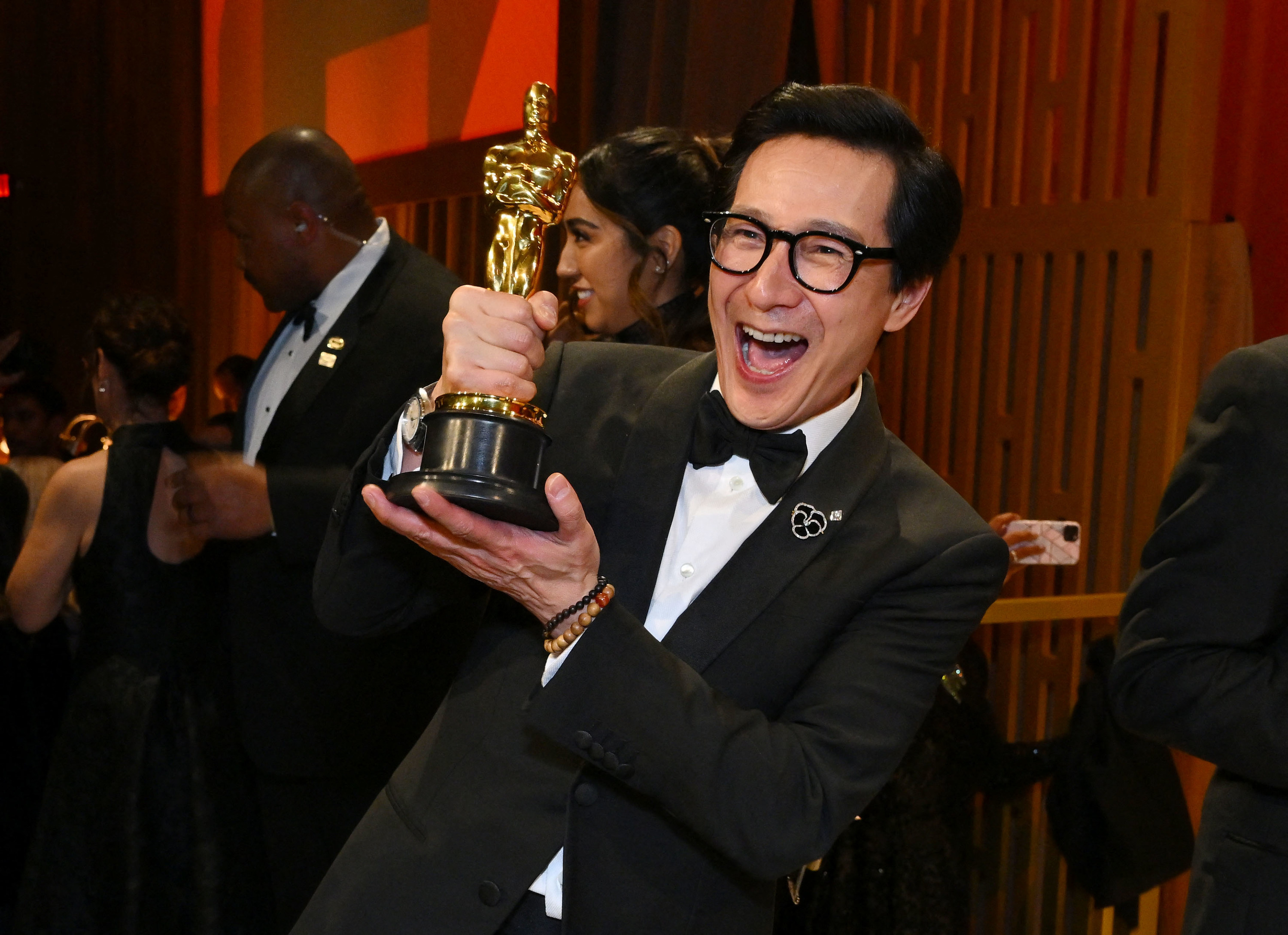 Ke Huy Quan smiles widely while holding up his Oscar