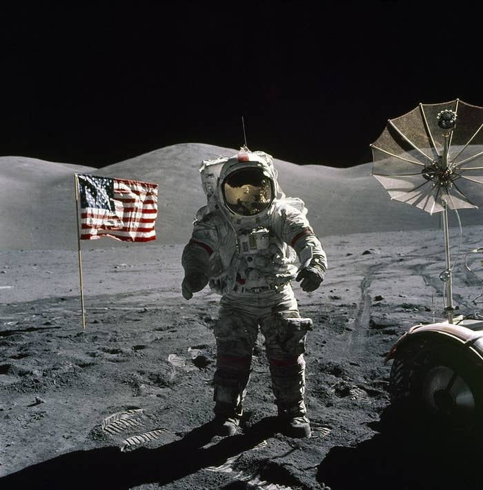 Man in a spacesuit standing on the moon with a US flag behind him