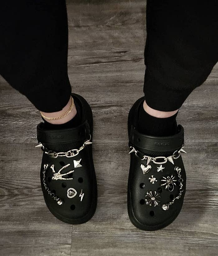 A pair of black platform crocs with silver charms on them,