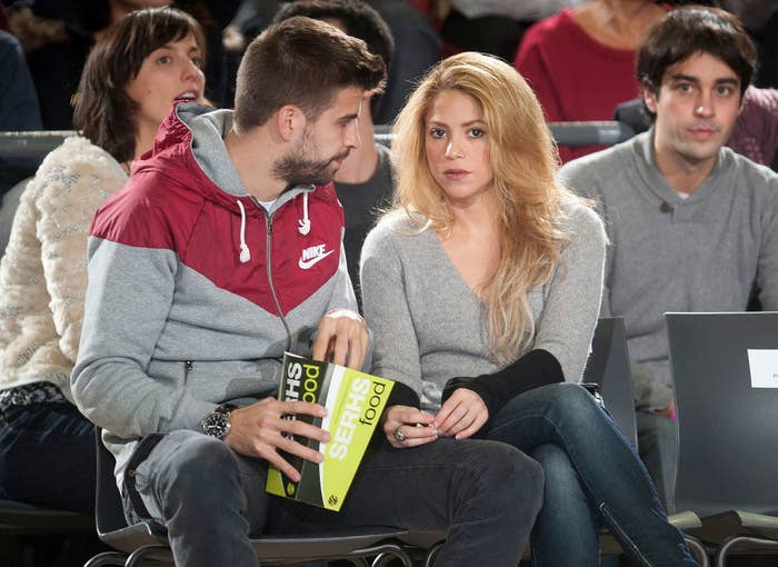 Gerard eating popcorn as he and Shakira sit court side at a sports event