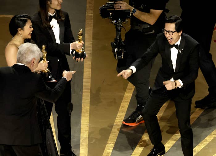 Ke Huy Quan and Harrison Ford point at each other on stage as Quan smiles after winning Best Picture