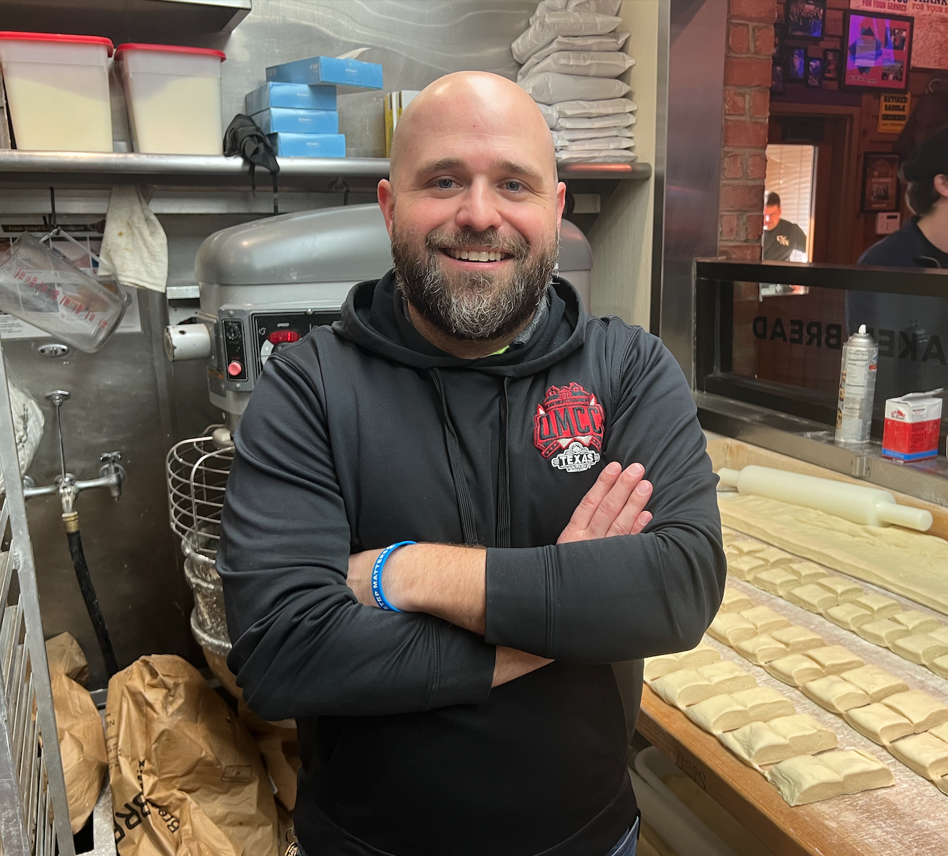 Kyle smiles as he stands behind a counter filled with rolls ready to be baked