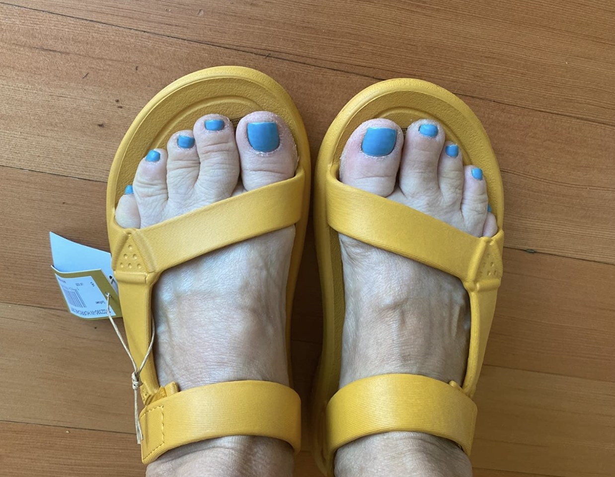 Someone with blue toenail polish wearing a pair or yellow Tevas sandals.