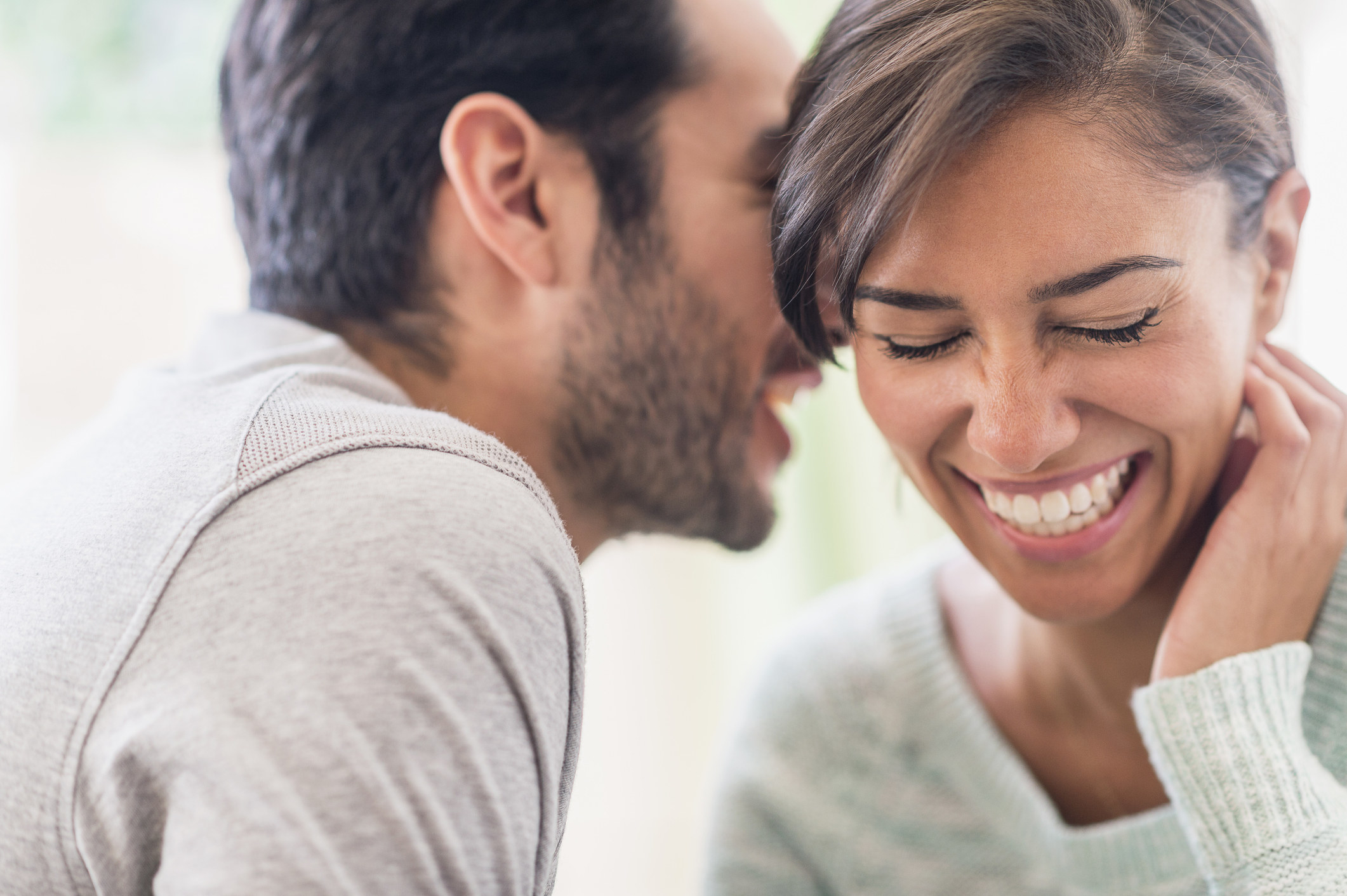 A man whispering in a woman&#x27;s ear as she laughs