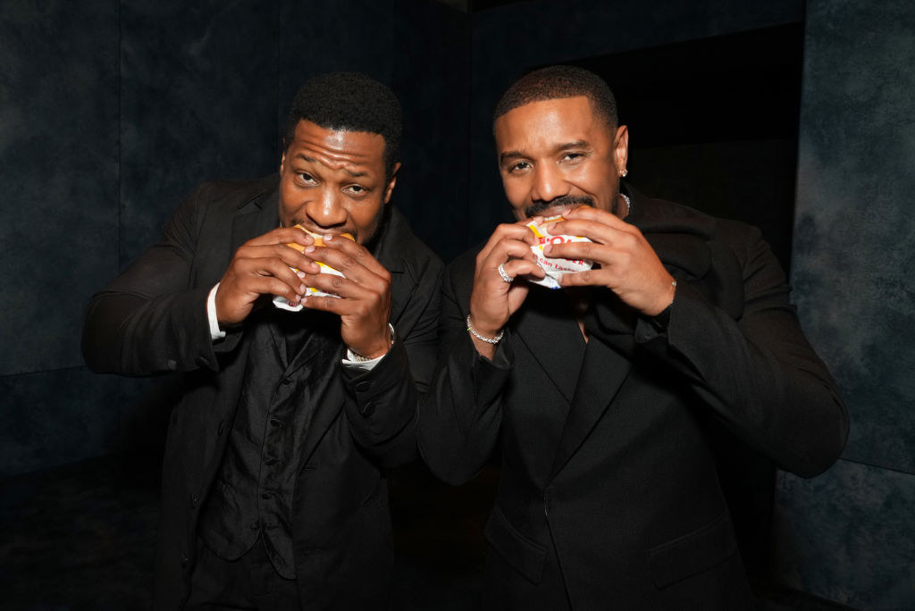 Jonathan Majors and Michael B. Jordan biting into burgers