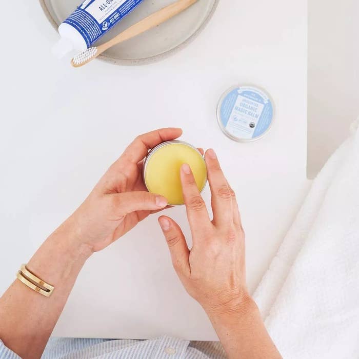 A model sticking their finger into the organic magic balm to apply