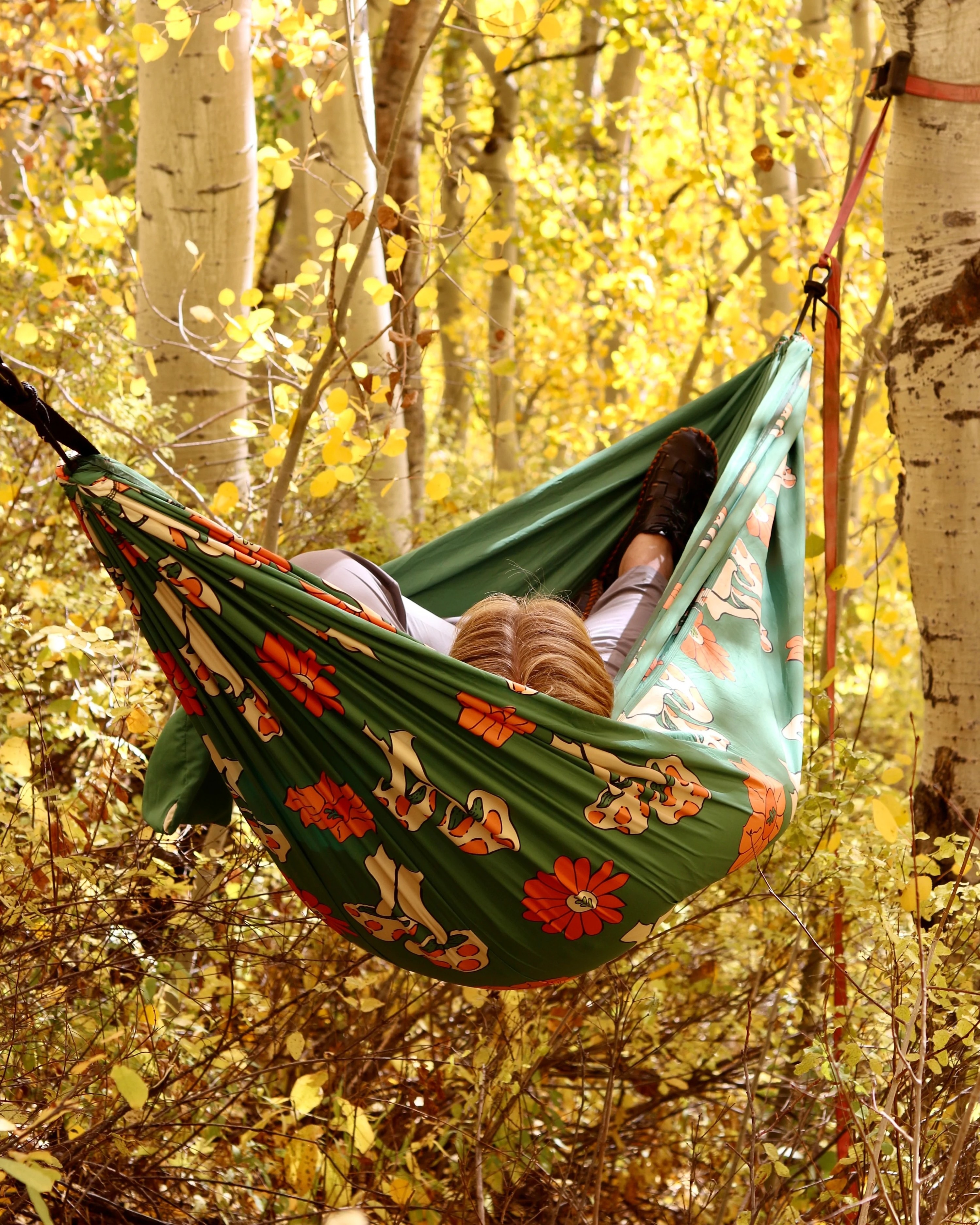 a model laying in the mushroom printed hammock in the trees