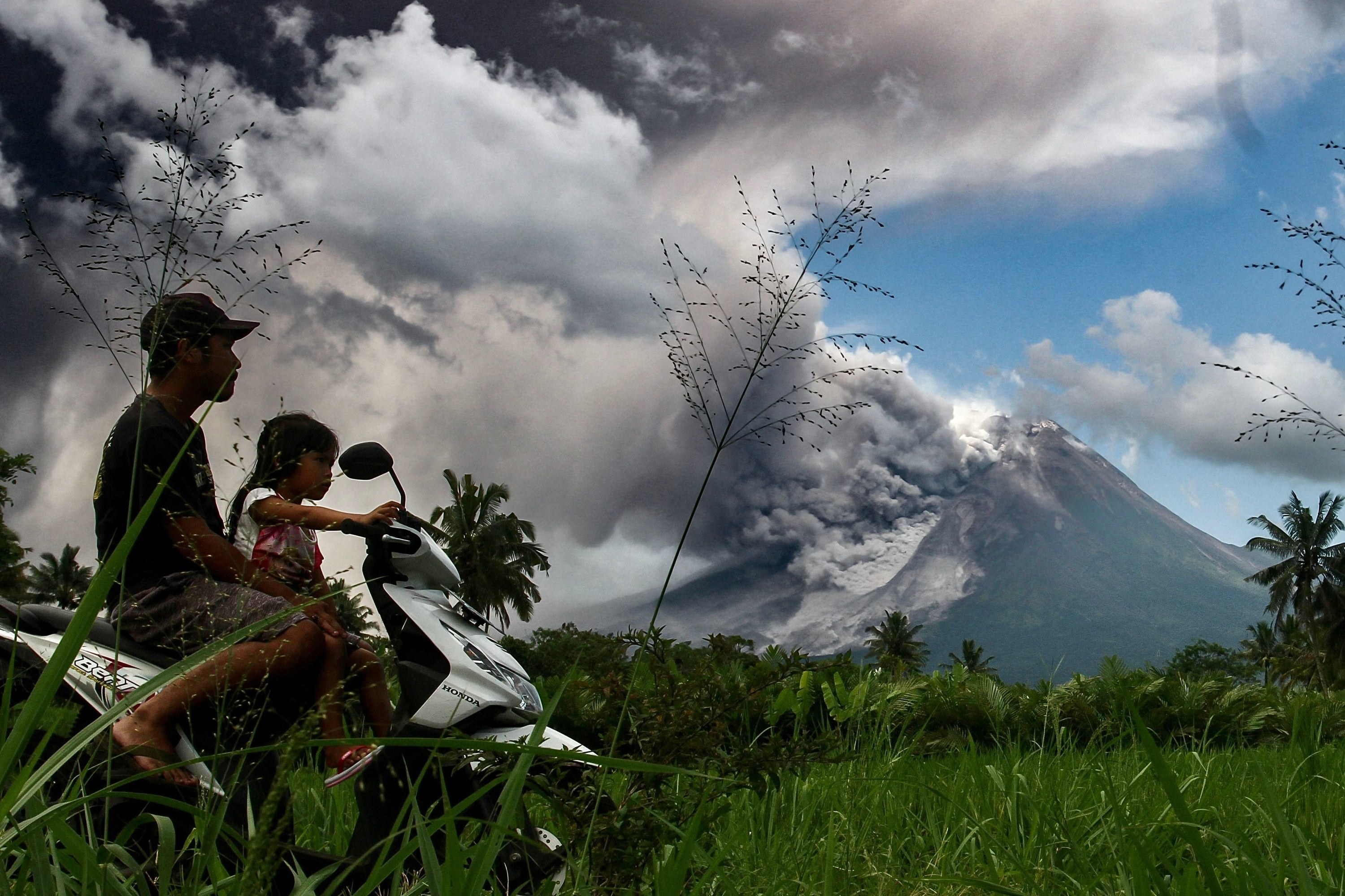 father and young daughter riding a motorbike with a smoking volcano in the background