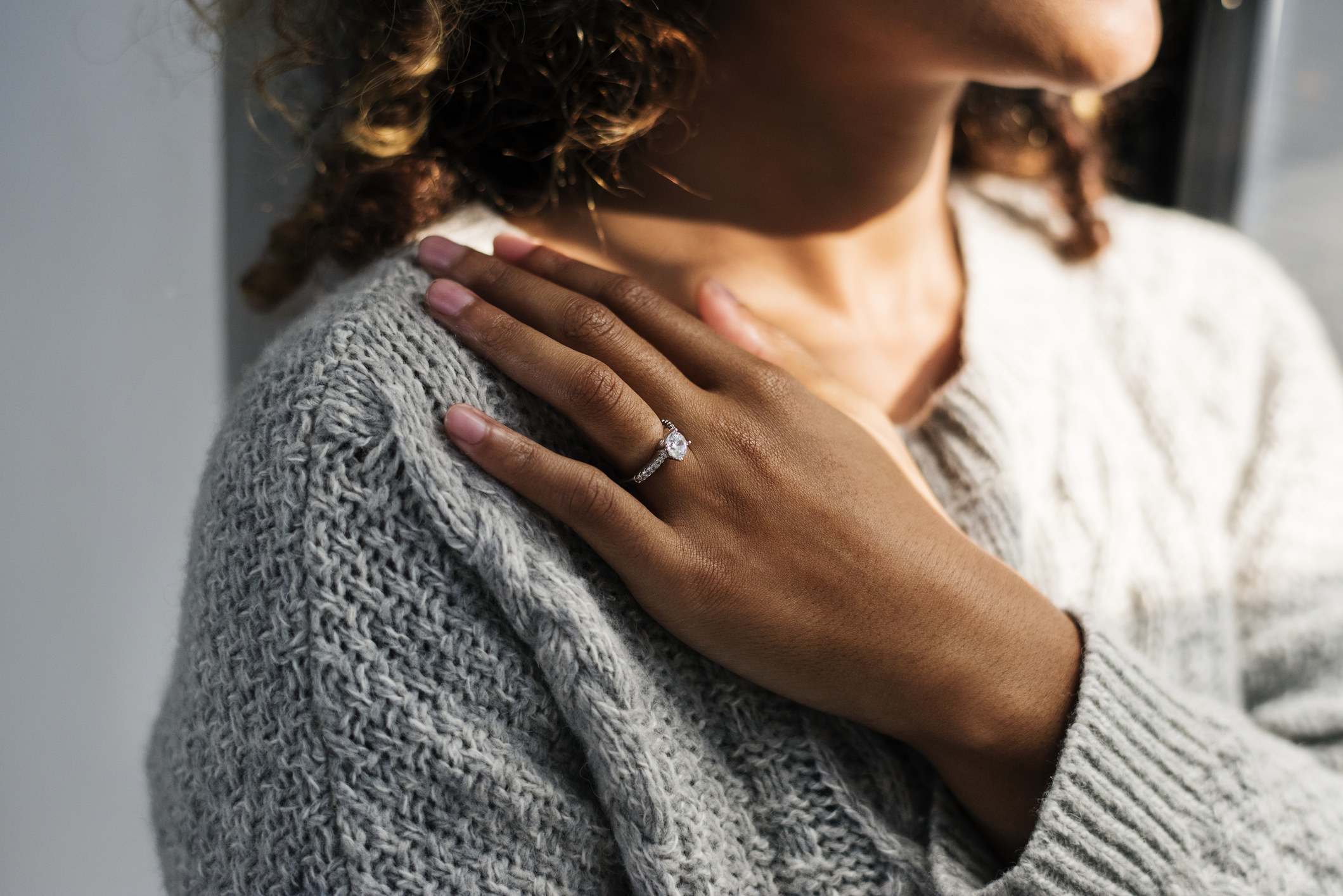 A woman touching her shoulder with a hand that has an engagement ring on it