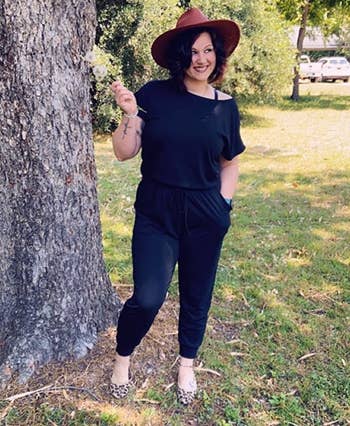 Reviewer's photograph of them wearing the jumpsuit successful the colour Black, styled with leopard people flats and a brownish reddish wide-brimmed fedora