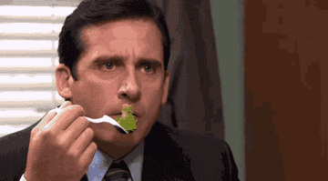 Michael Scott eating broccoli at his desk.