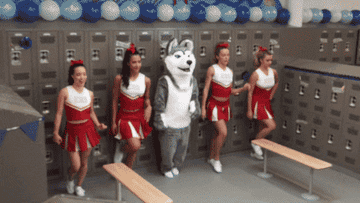 Cheerleaders dancing with a school mascot.