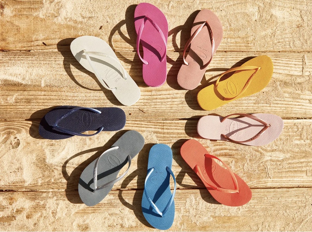 A circle of Havaiana flip flops in white, pink, rose pink, yellow, light pink, orange, blue, grey, navy, and white on a wooden background