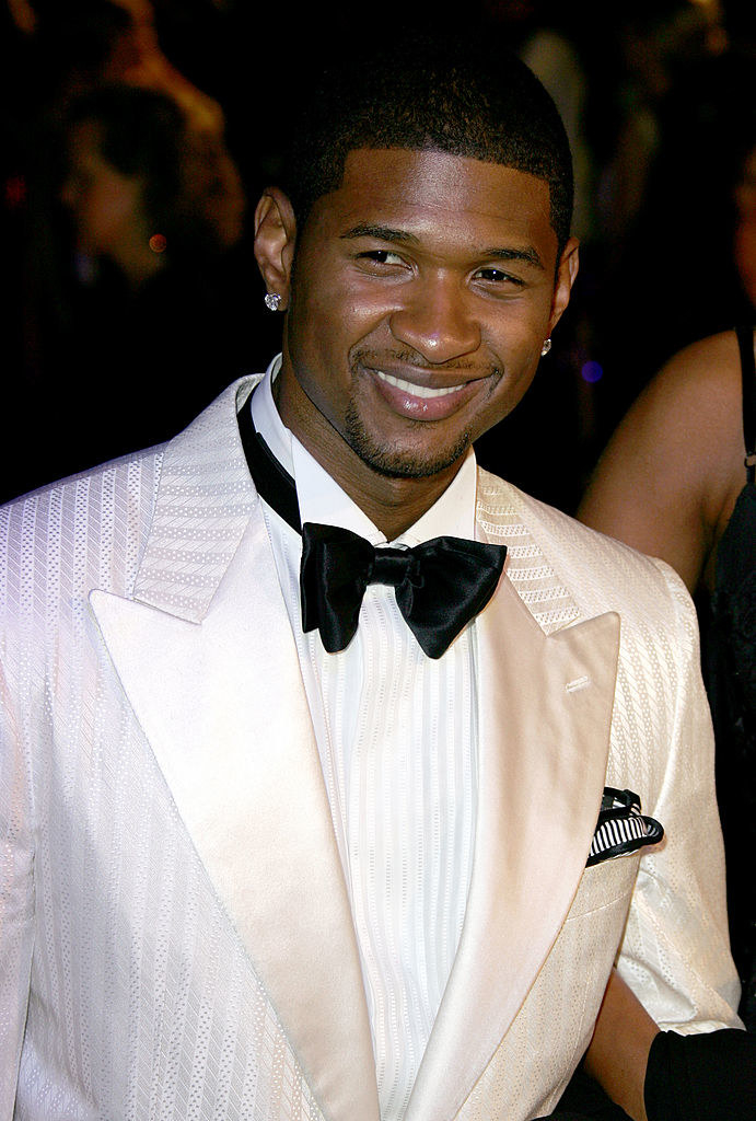 A younger dapper Usher in a tuxedo and two diamond stud earrings. He&#x27;s smiling as he looks to the side