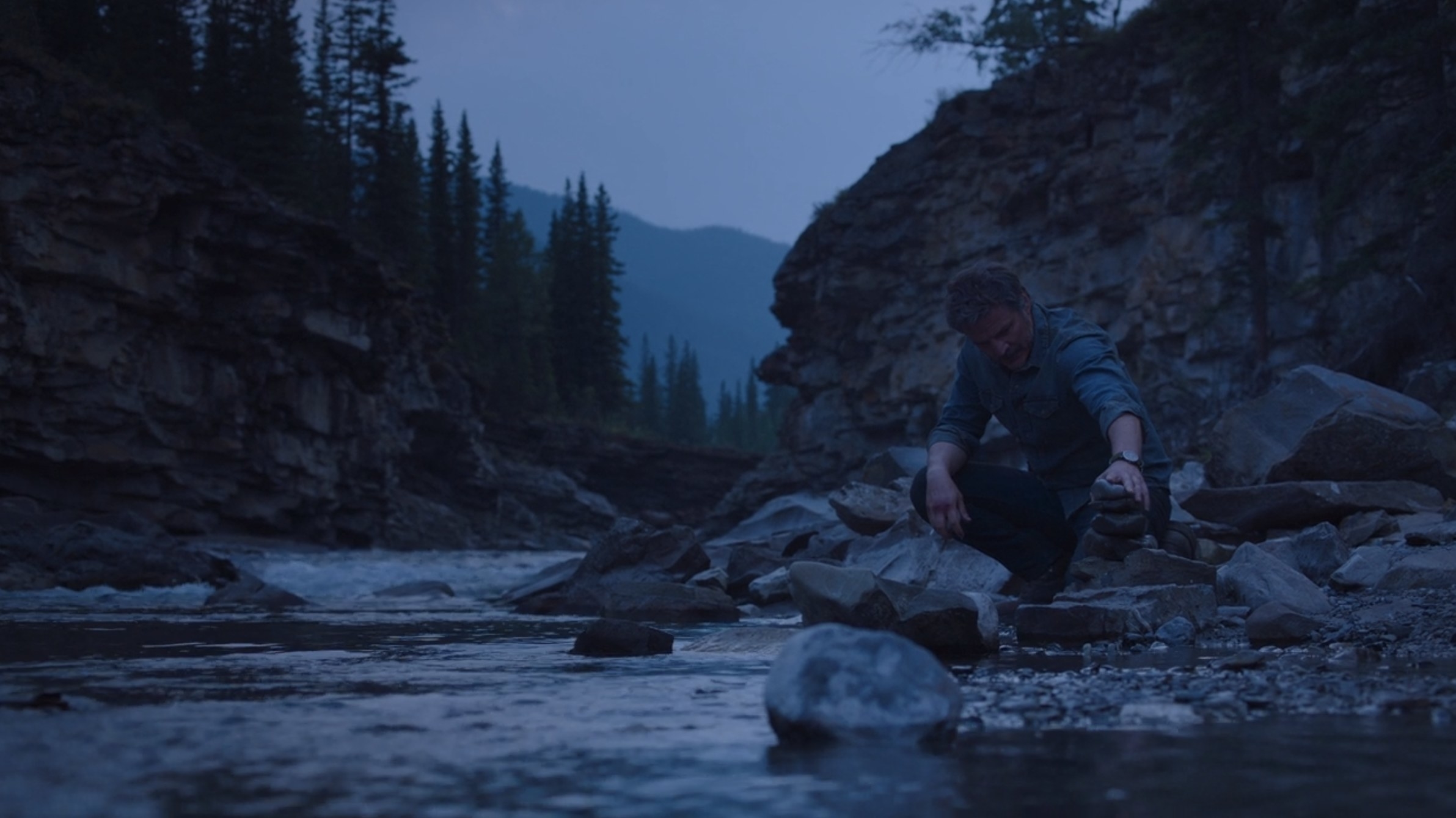 joel stacking rocks near the river on the last of us