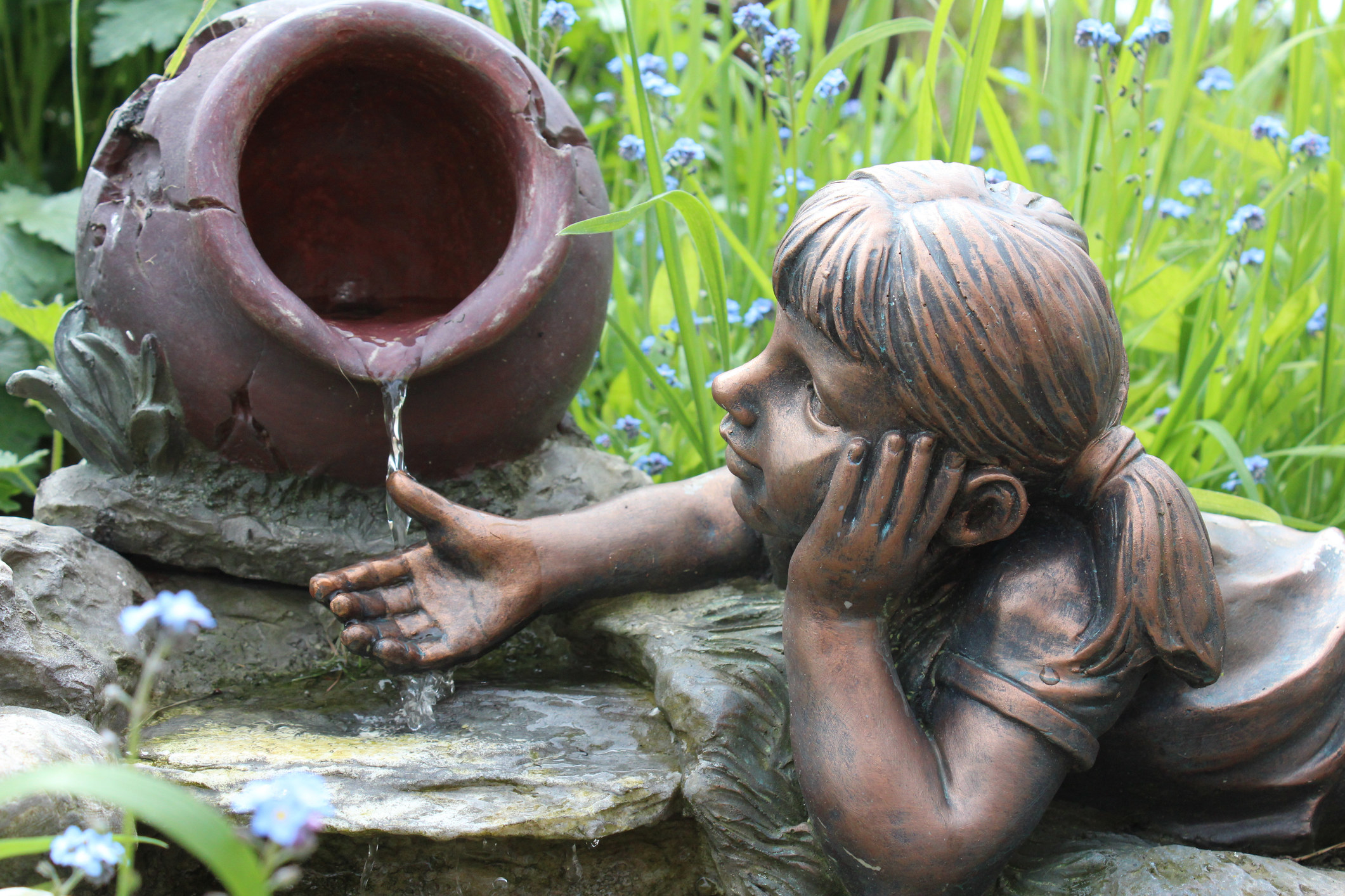 A water garden sculpture of a little girl with her hand under a pot that is spilling water