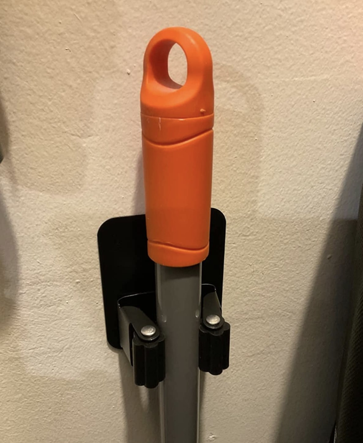 reviewer photo showing the broom holder affixed to their wall holding and orange broomstick with ease