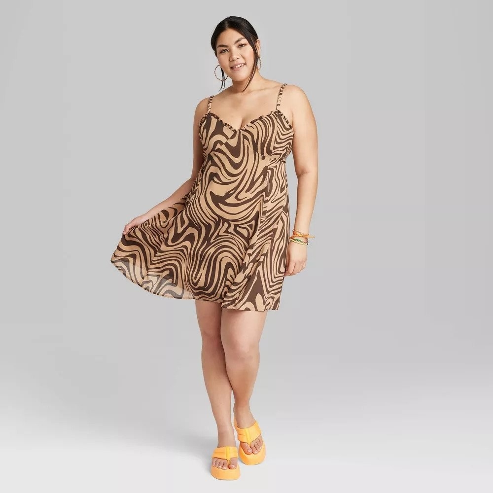 Model wearing brown and beige design mini slip dress with orange flip-flops
