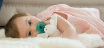 A baby model sucking on the pacifier and snuggling the stuffed lamb