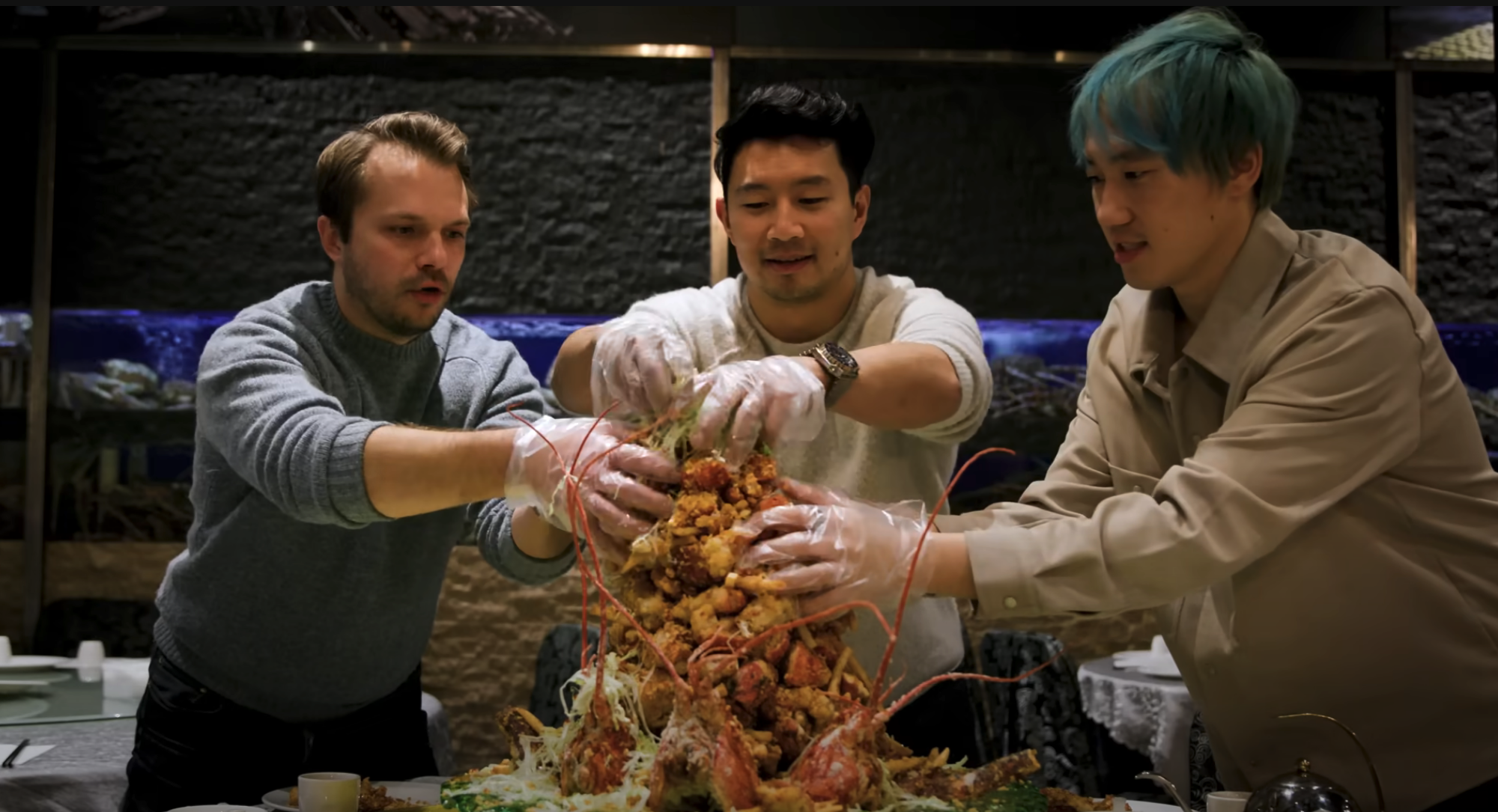 Three men wearing gloves start grabbing a tower of lobster