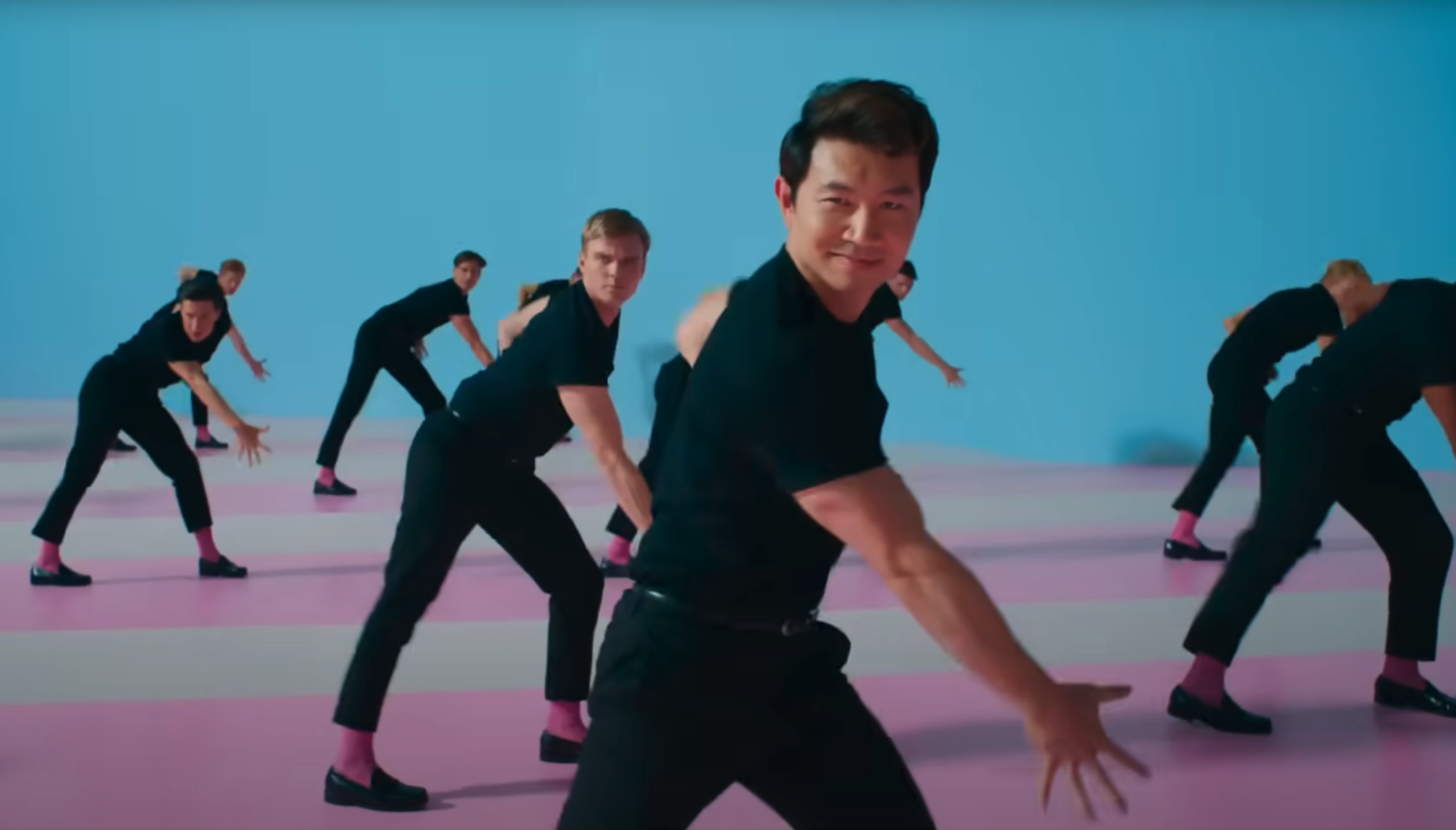 Men dance in matching outfits on a pink and blue background