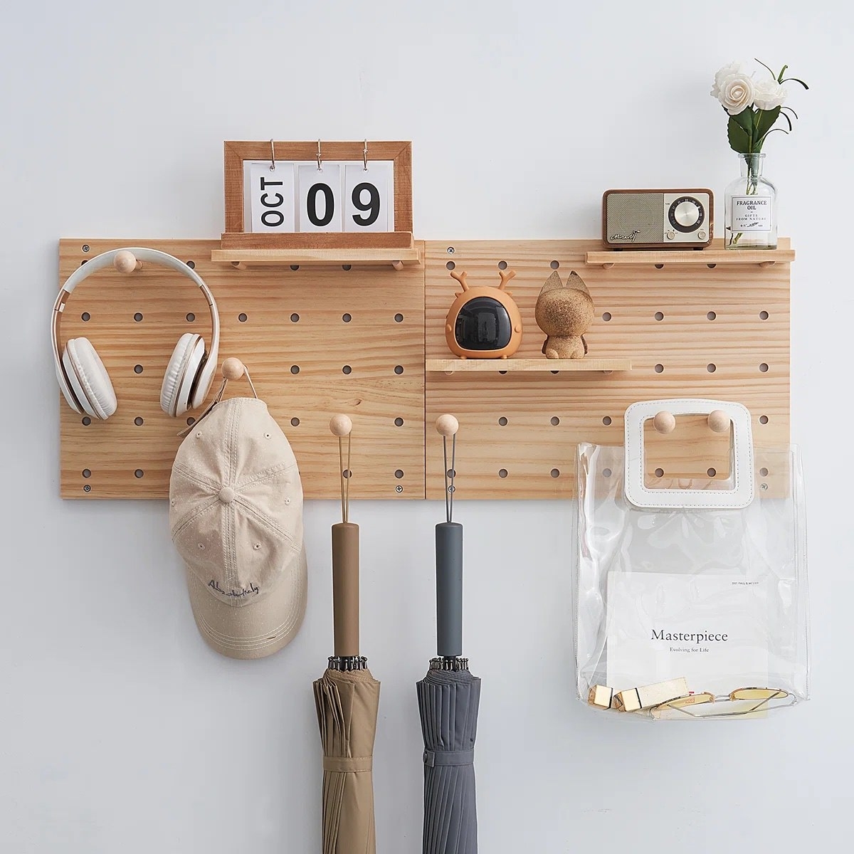 a wooden peg board holding hats, umbrellas, white headphones, and knickknacks against a white wall