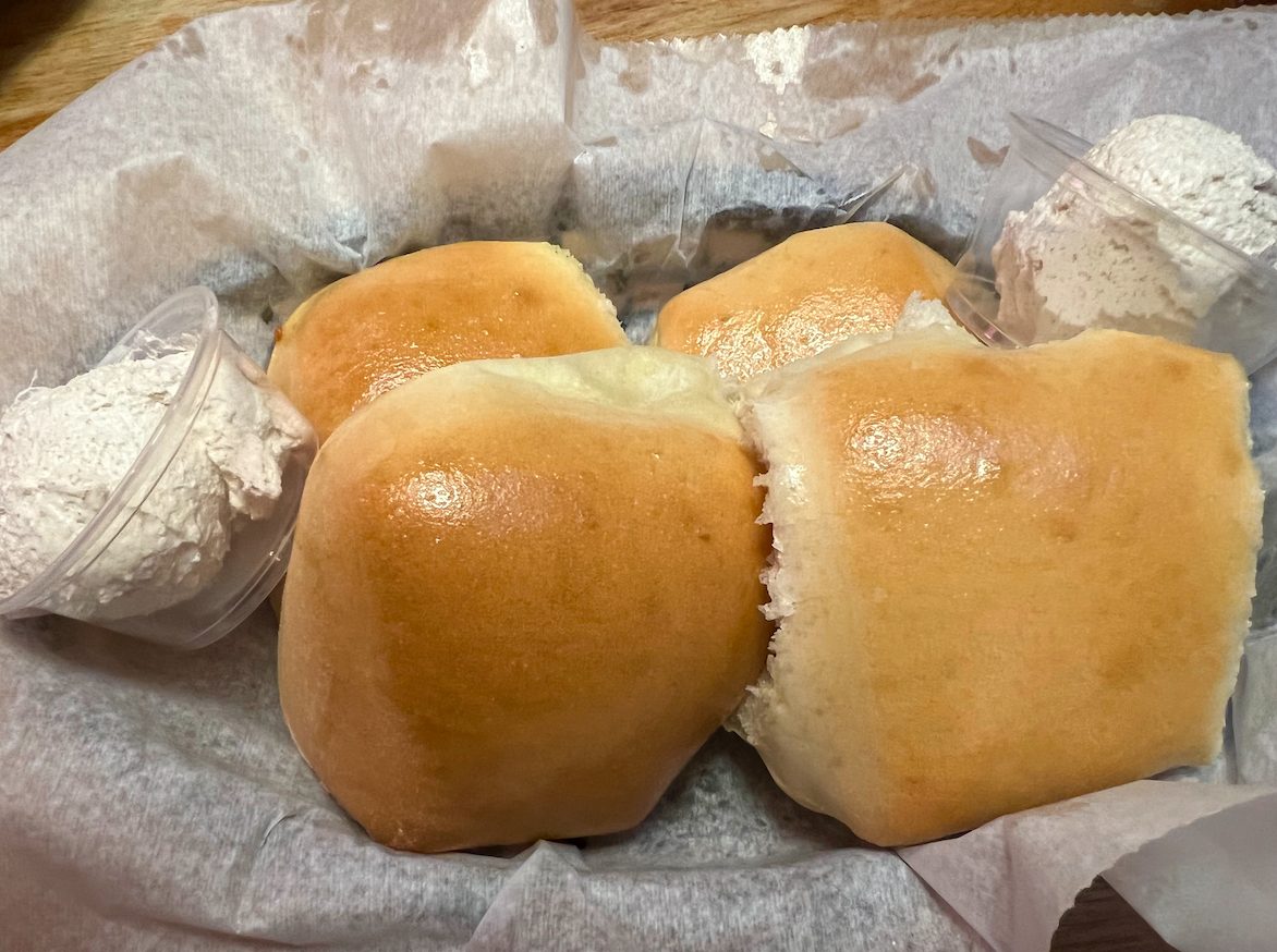 A basket of four rolls with two small containers of whipped butter