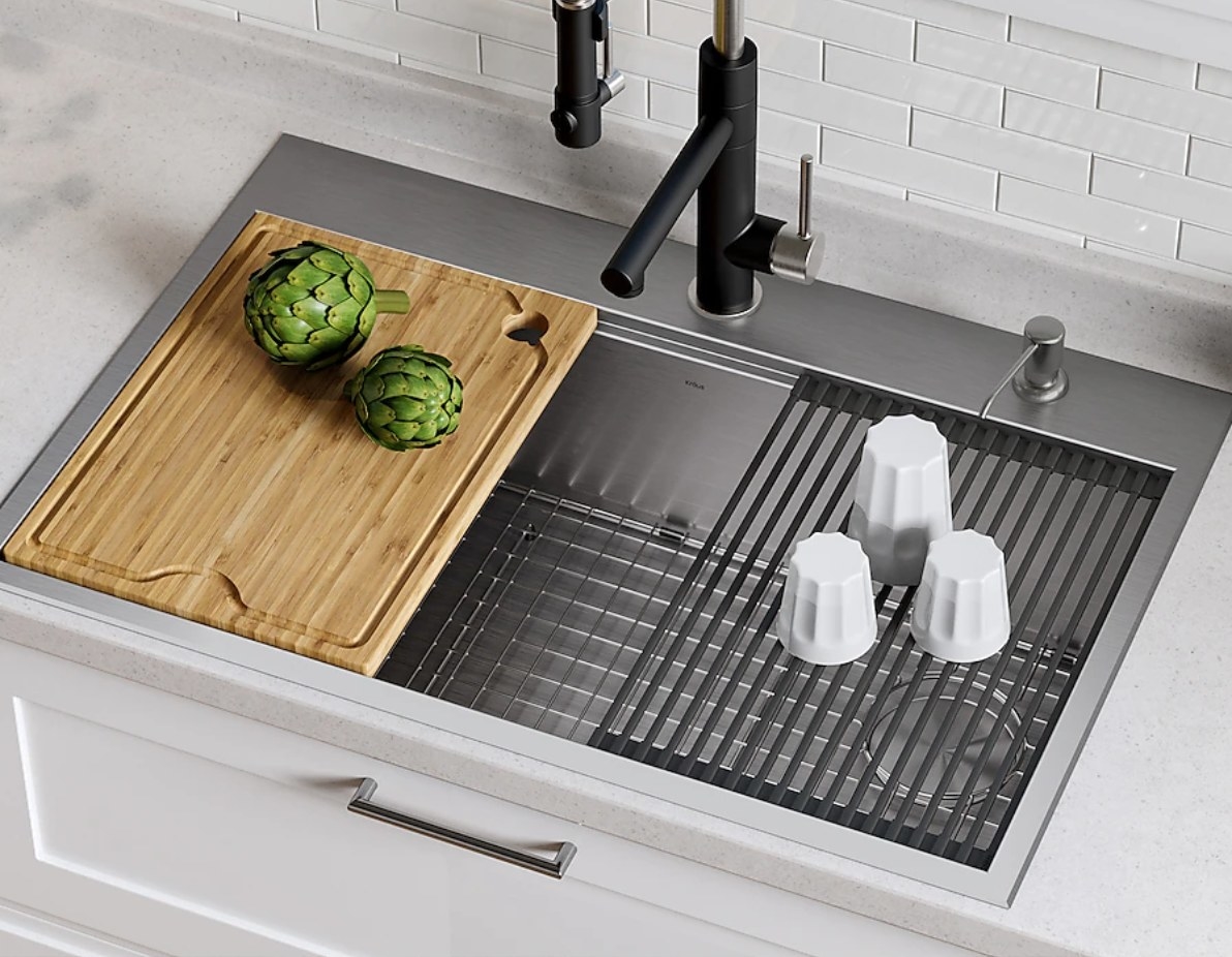 a stainless steel sink with a cutting board and drainboard under artichokes and salt and pepper shakers