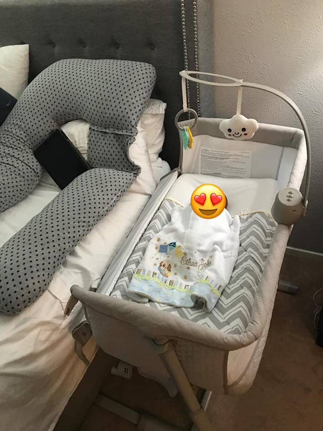 reviewer's bedside sleeper connected to their bed with baby in it