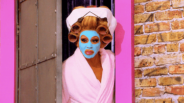 RuPaul closing the door while wearing a face mask, hair curlers, and a robe