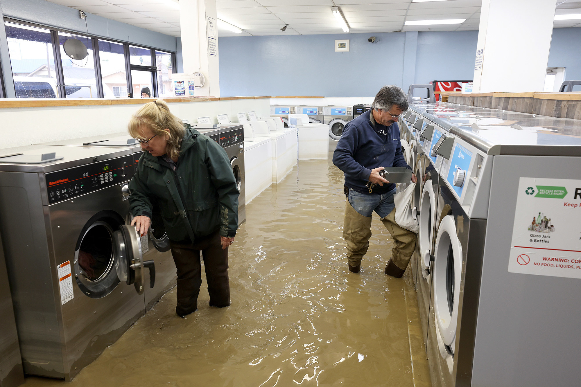 two people examine laundry machines at a flooded laundromat